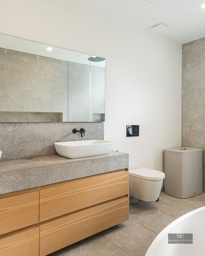 Salle de bain de luxe avec deux vasques sur un plan en pierre, meubles en bois et grand miroir.