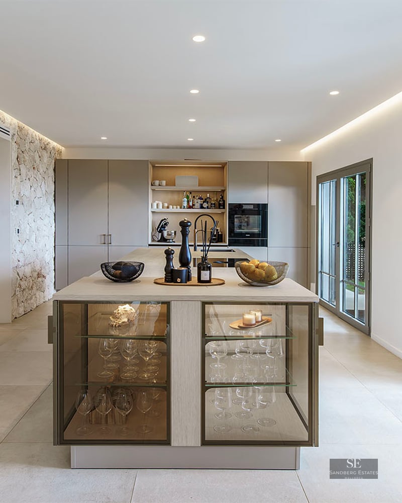 Spacious contemporary kitchen featuring a large island, integrated wine cooler, natural stone wall, and garden access.