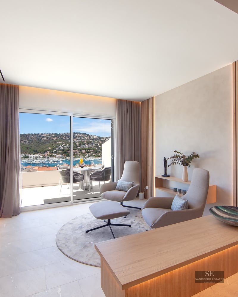 Modern lounge with wood slats, designer chairs, and a sliding glass door revealing a stunning Mediterranean harbor view.