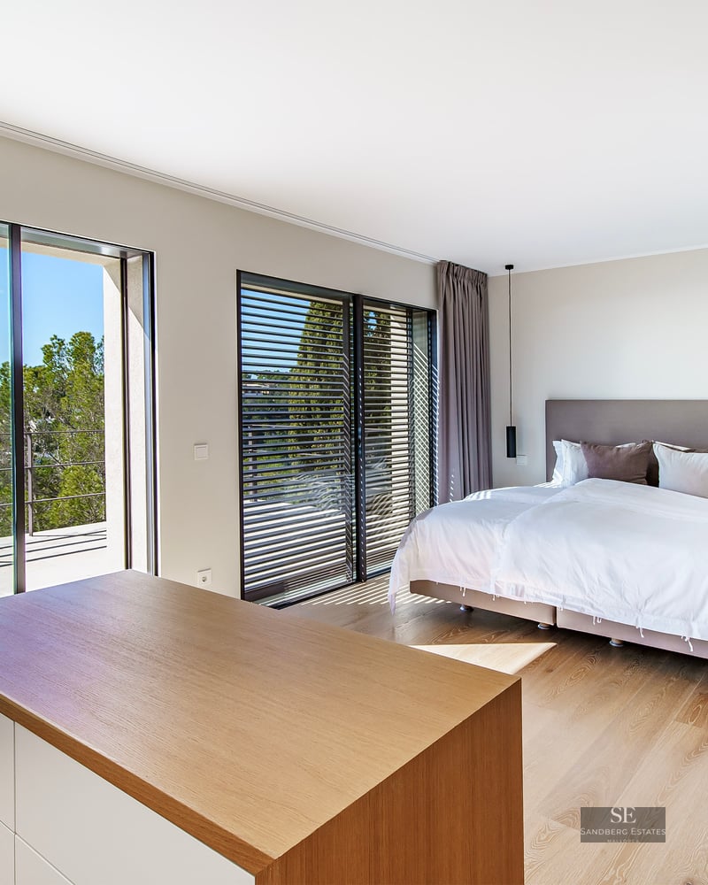 Bright master bedroom featuring wooden floors, a large bed, and floor-to-ceiling sliding glass doors opening to a terrace.
