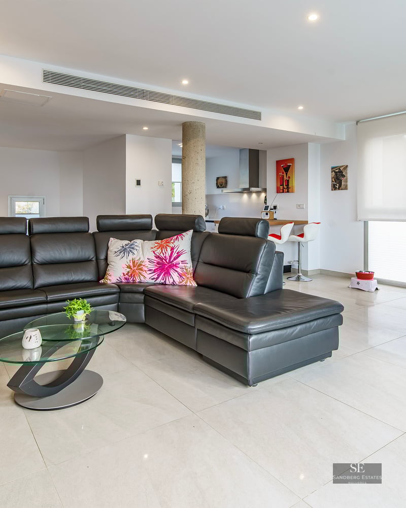 Spacious living room with a large black leather sofa, glass coffee table, and a modern dining area in an open-plan layout.