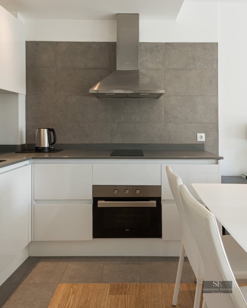 Cuisine blanche moderne avec crédence grise, appareils en inox et table à manger blanche.