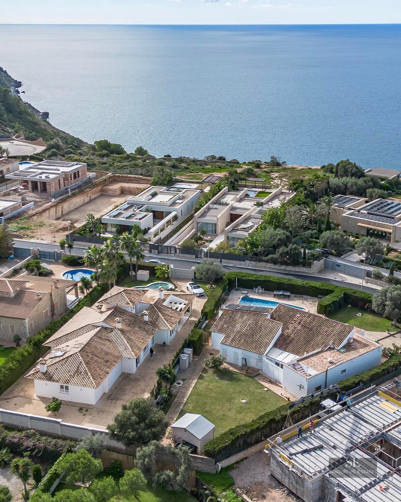 High-angle aerial view of an exclusive coastal residential area with Mediterranean villas, private pools, and sea views.