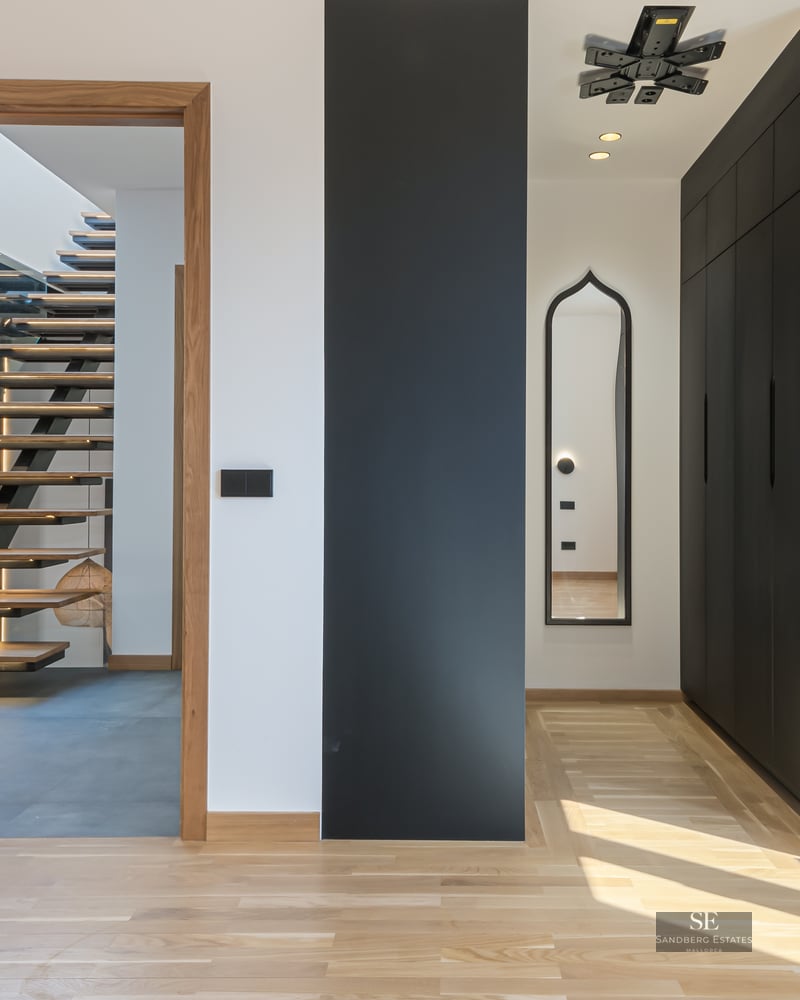 Modern hallway with light wood floors, black built-in closets, and an open door viewing a floating wooden staircase.