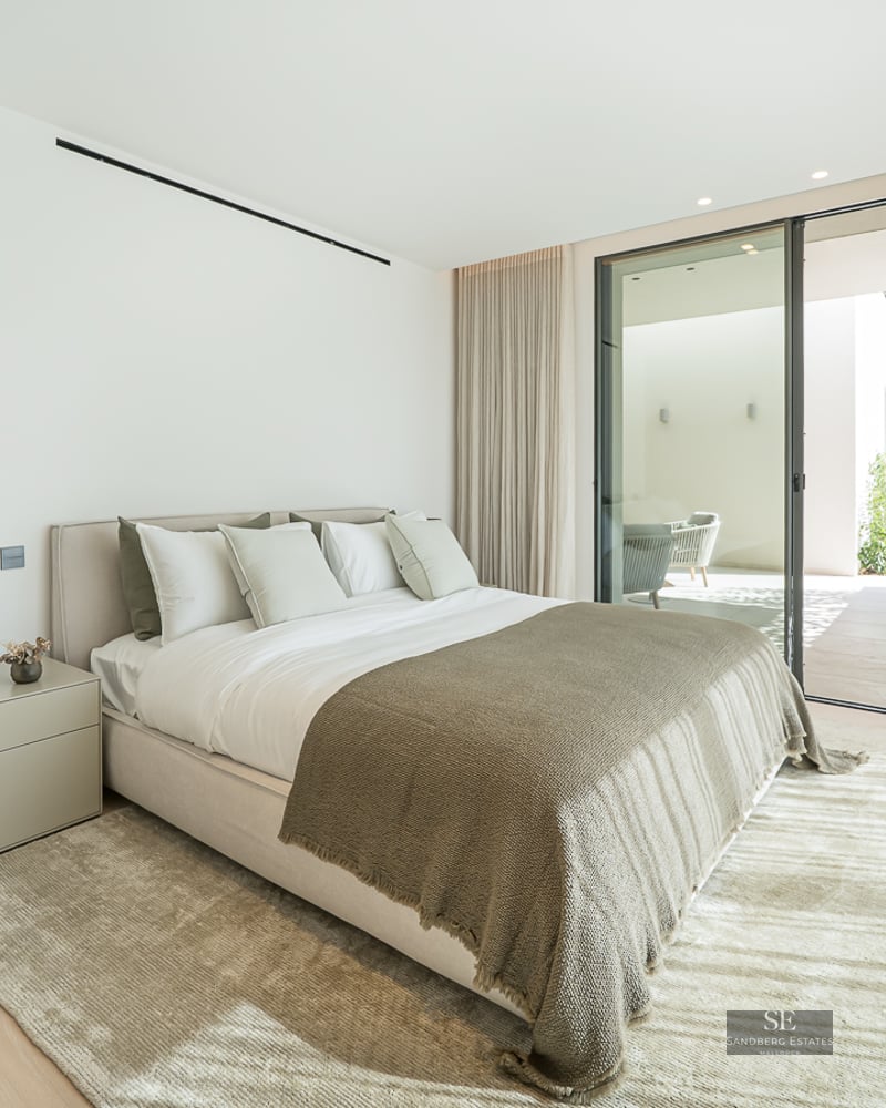 Modern master bedroom featuring a large bed, light wood floors, and sliding glass doors leading to a private terrace.