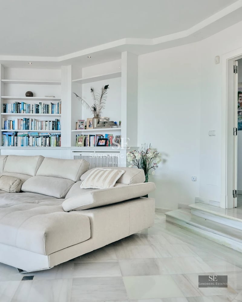 View of a modern pool with a minimalist design villa in the background. Large windows, terraces, and lush vegetation.