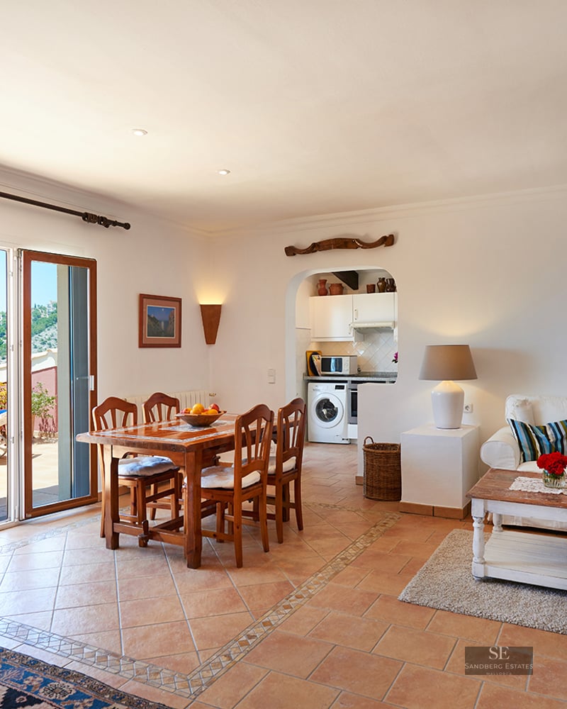 Bright open-plan living and dining room with terracotta floors opening onto a sunny terrace with hillside views.