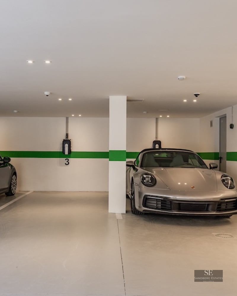 Bright underground parking with a black Mini and silver Porsche parked next to electric vehicle charging stations.