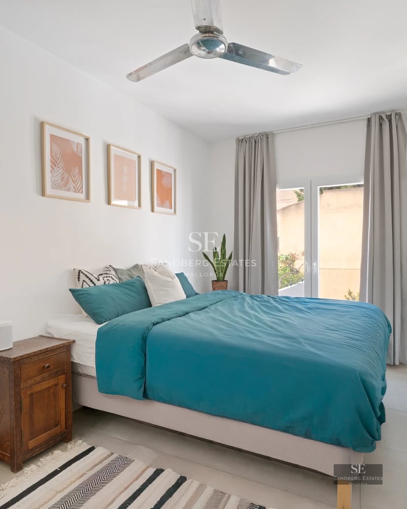 Spacious living room with floor-to-ceiling windows, light wood floors, and modern furniture. Views of lush garden and shimmering pool.