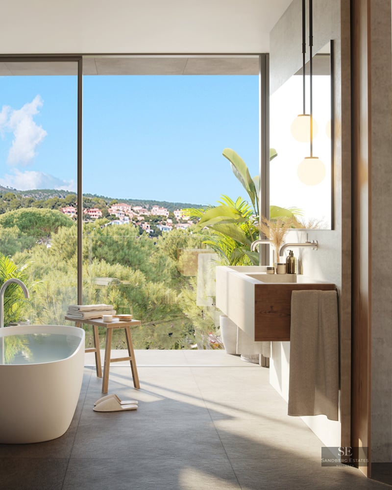 Luxury master bathroom featuring a freestanding tub, floating wood vanity, and floor-to-ceiling windows with forest views.