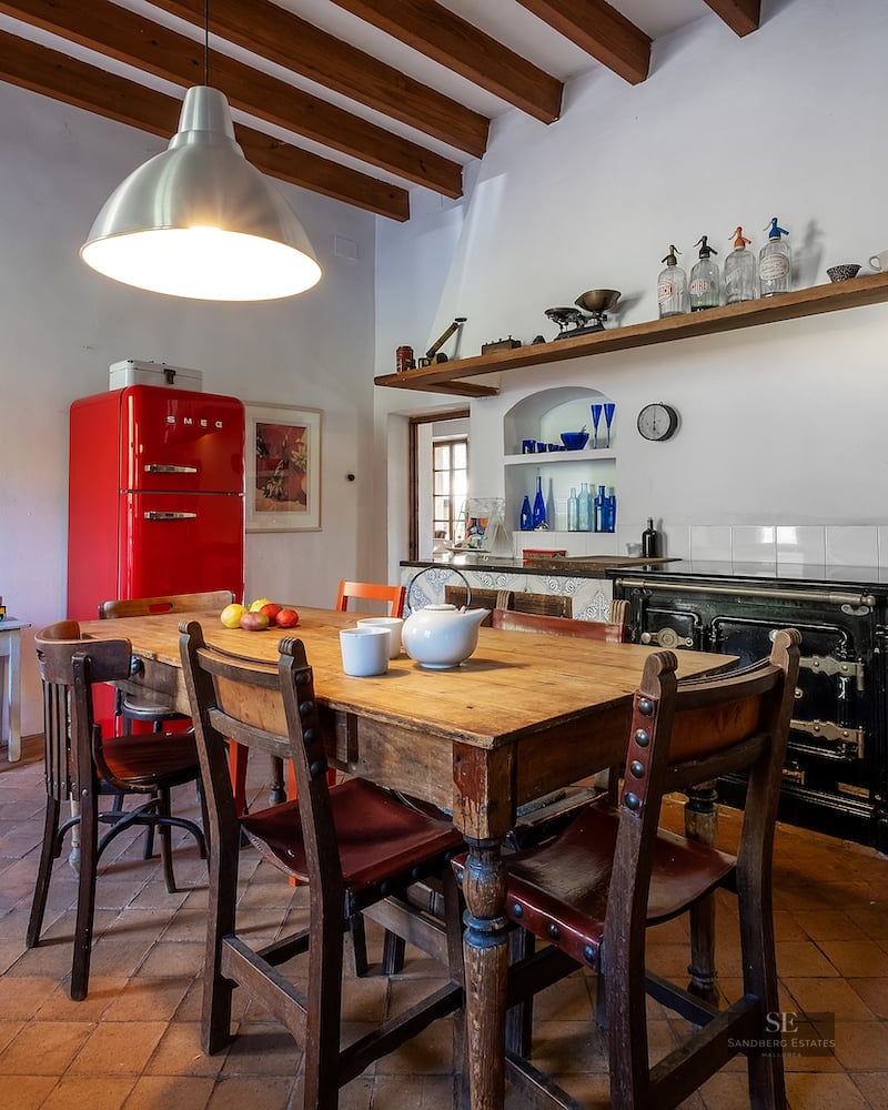 Traditional kitchen with terracotta floors, wooden beams, a rustic dining table, and a vibrant red retro refrigerator.