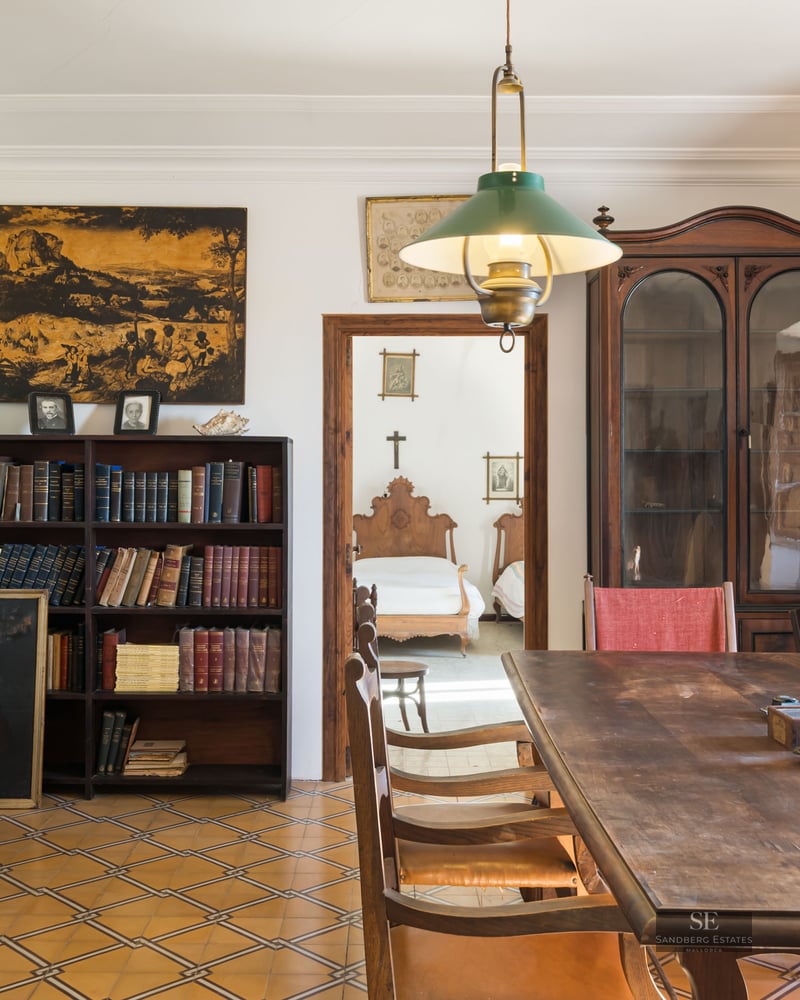 A classic room featuring a large wooden table, floor-to-ceiling bookshelves, and patterned tile flooring.