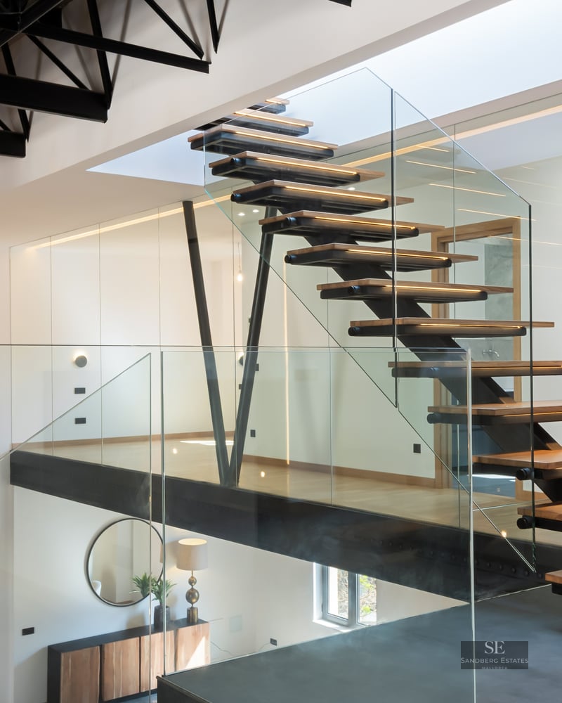 Wood and glass staircase with black metal structure and woven pendant lights in a modern interior.