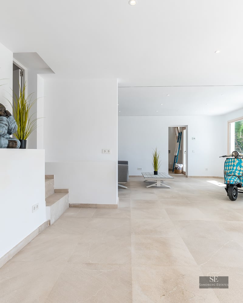 Spacious white interior with light stone floors, decorative monk statues, and a blue vintage scooter.