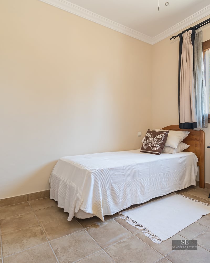Small bedroom with single bed, tiled floors, wooden window frame, and a decorative electric fireplace heater.