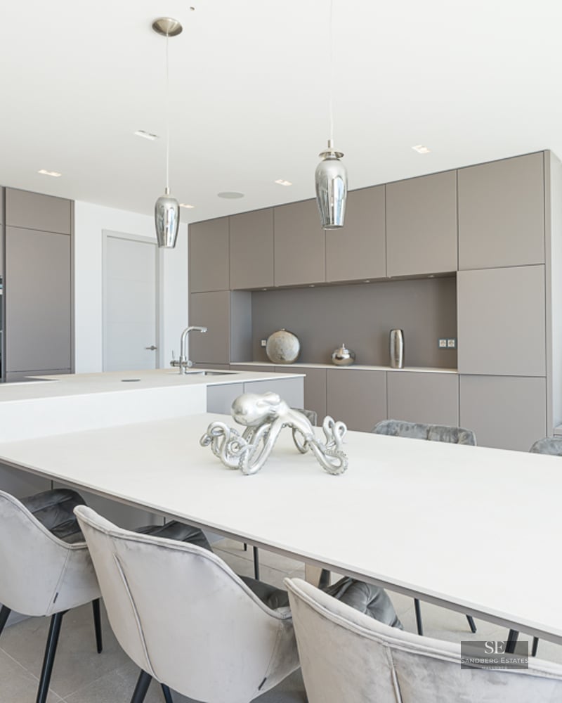 Contemporary kitchen with taupe cabinets, a large white island, and grey velvet dining chairs.
