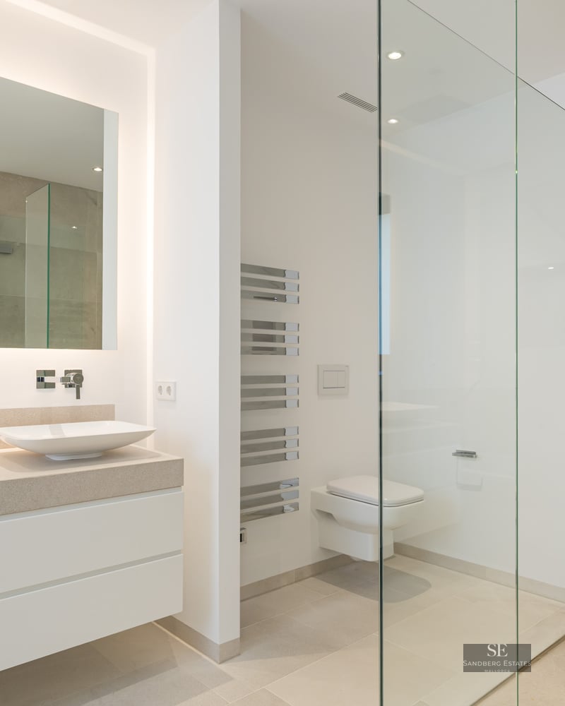 Modern master bathroom featuring a double white vanity, large backlit mirror, and a walk-in glass shower with stone tiles.