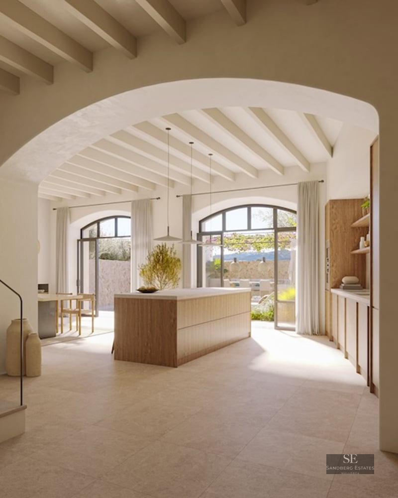 Minimalist kitchen with wooden island, beamed ceiling, and large arched doors opening to a terrace.