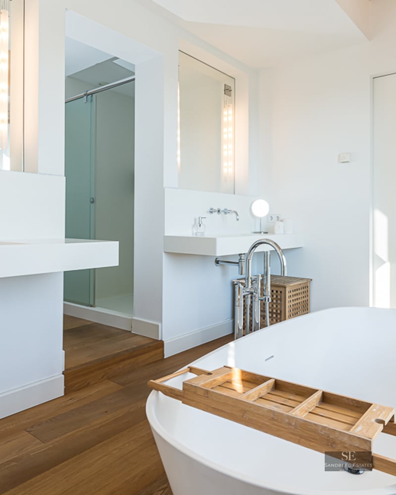 Bright master bathroom featuring a white freestanding bathtub, wooden floors, and modern floating sinks.