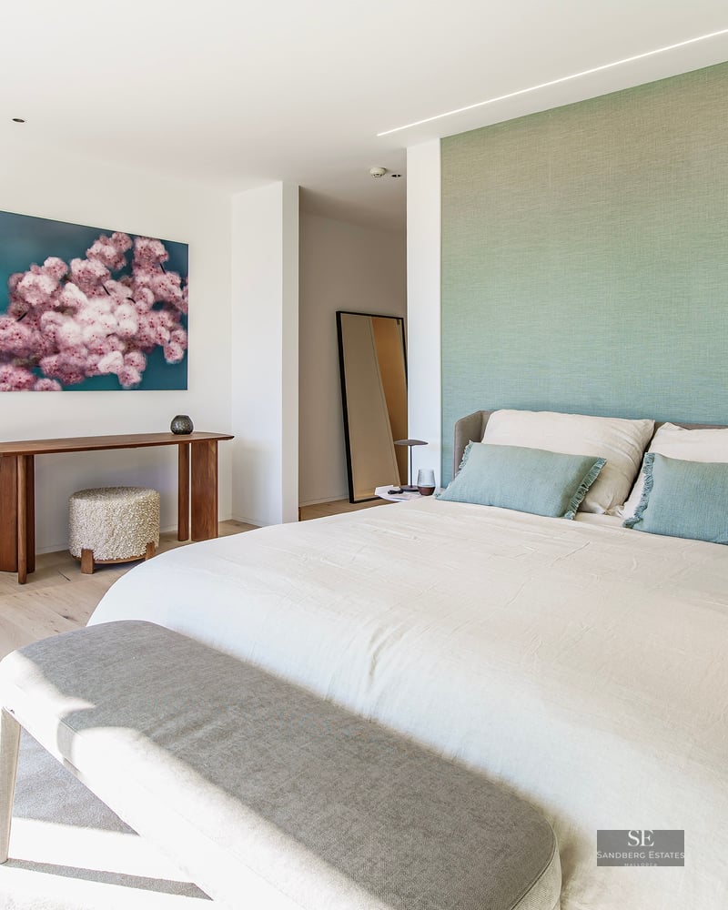 Bright master bedroom featuring a sage green wall, large bed, and designer furniture on light wood floors.