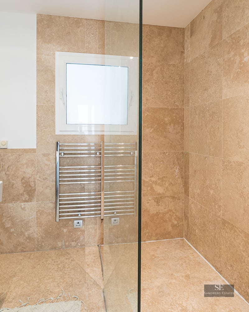 Modern bathroom featuring beige travertine tiles, a glass walk-in shower, a heated towel rack, and a white vanity sink.