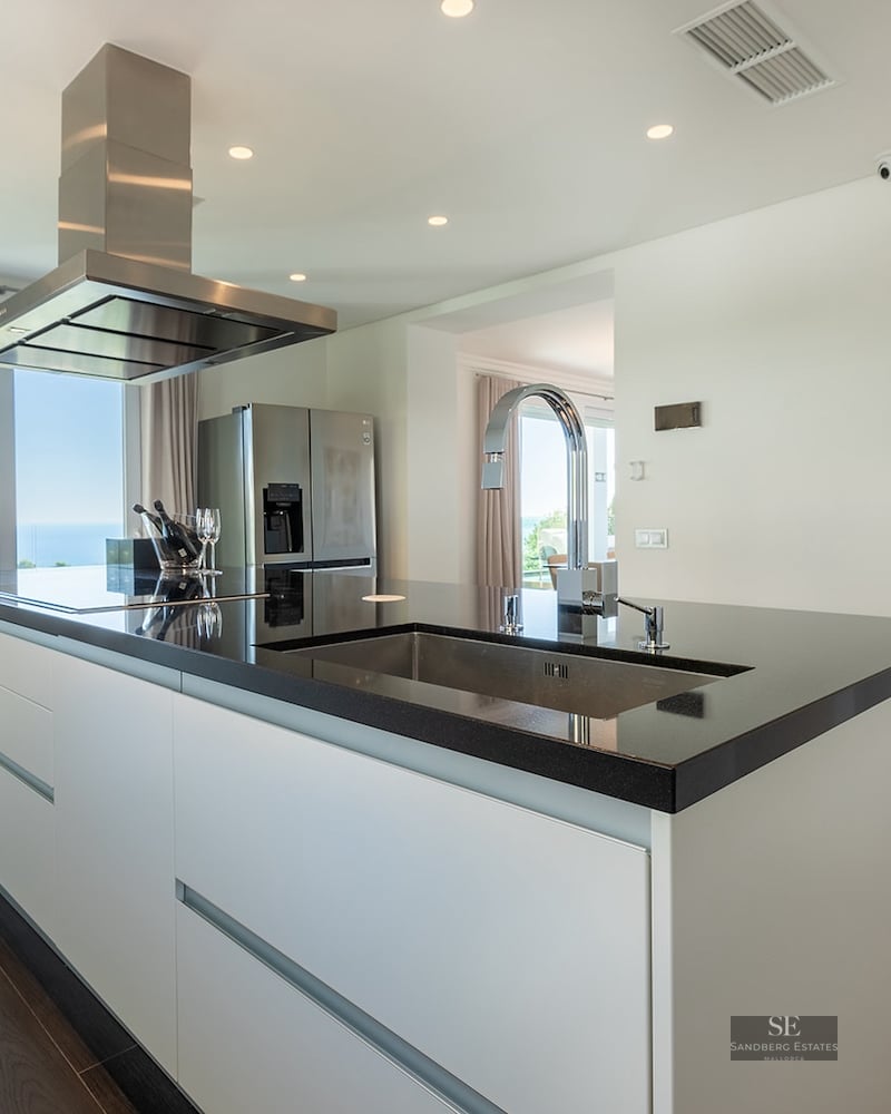 Modern kitchen featuring a black island, stainless steel hood, and floor-to-ceiling windows with a sea view.