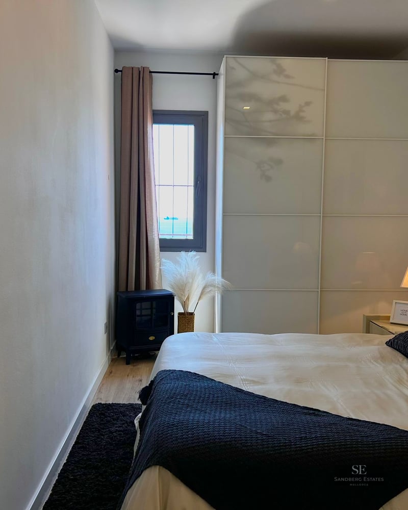 Modern bedroom featuring a large white wardrobe, a bed with dark pillows, and a small window with a sea view.