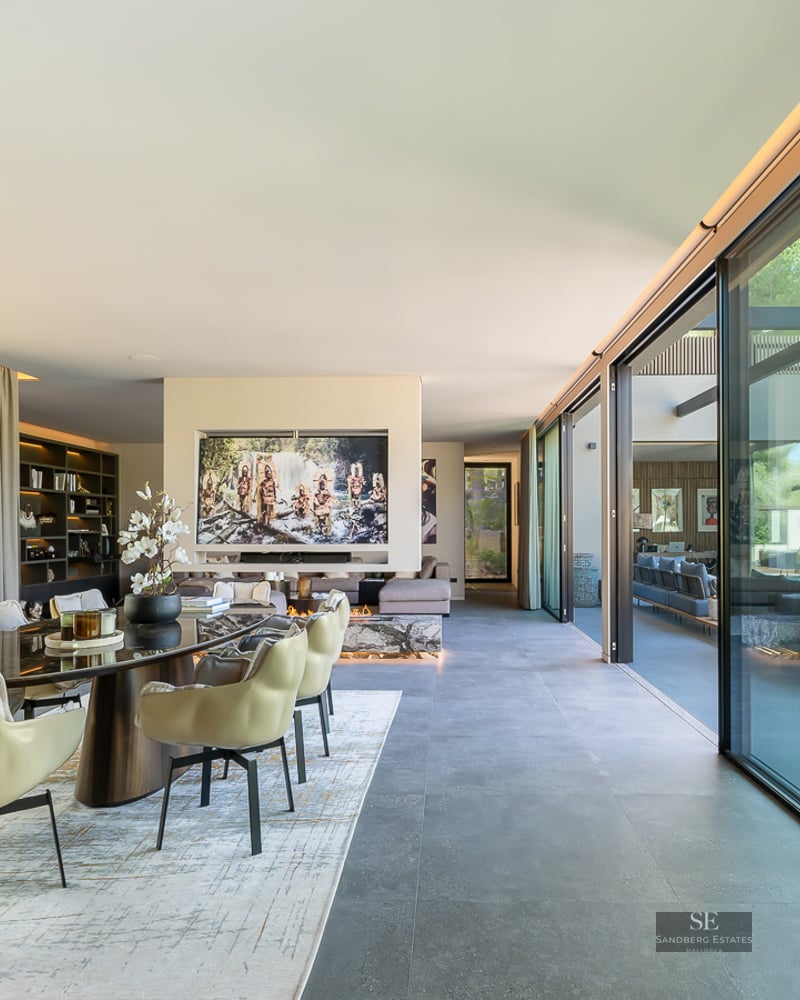 Spacious modern dining room with large floor-to-ceiling glass doors, elegant beige chairs, and garden views.