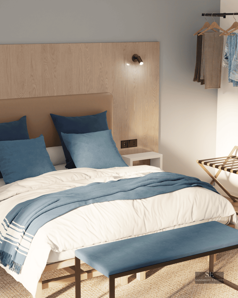 Une chambre moderne avec tête de lit en bois, oreillers bleus, banc bleu et miroir ovale sous une lumière naturelle.