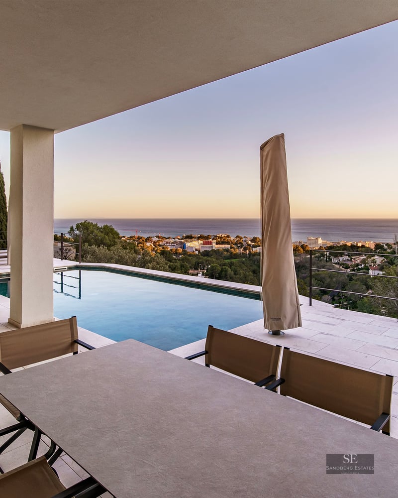 Modern terrace with an infinity pool, outdoor dining area, and panoramic sea views at sunset.