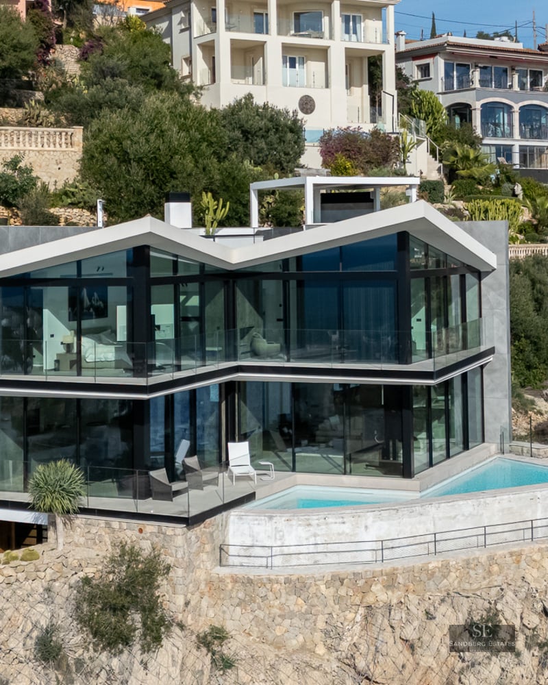 Modern glass villa built into a rocky hillside featuring an angular roof and a small infinity pool on the terrace.