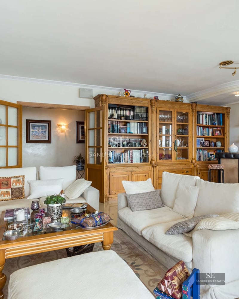 Large living room with white sofas, a massive wooden bookcase, a home bar area, and a dining table.