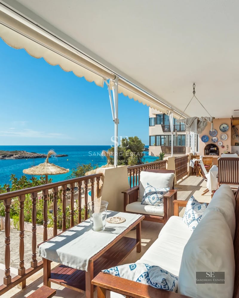 A wooden terrace with white sofas and a dining table overlooking a turquoise sea and a small island.