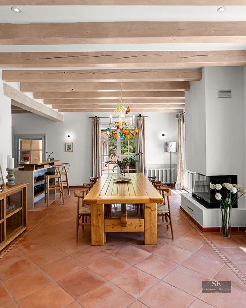 Large dining area featuring a wooden table, terracotta tile floors, exposed ceiling beams, and terrace access.