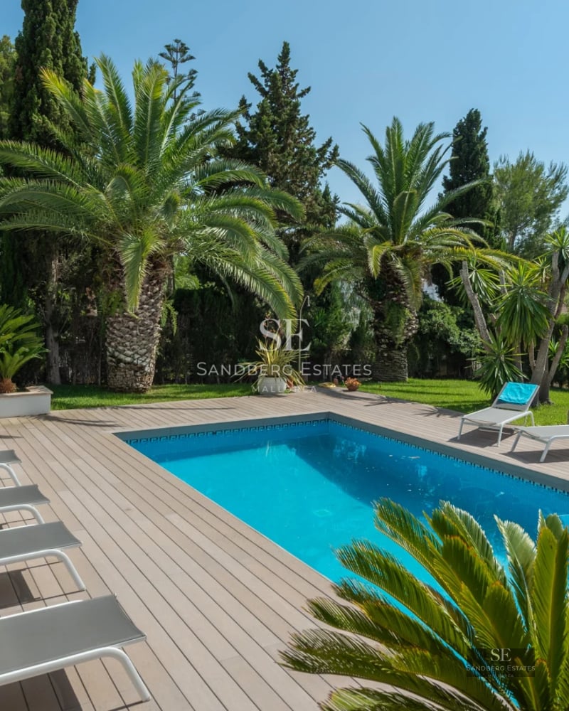 Exterior view of modern villa with infinity pool, wooden terrace, large glass windows, and lush garden. Contemporary architectural design.