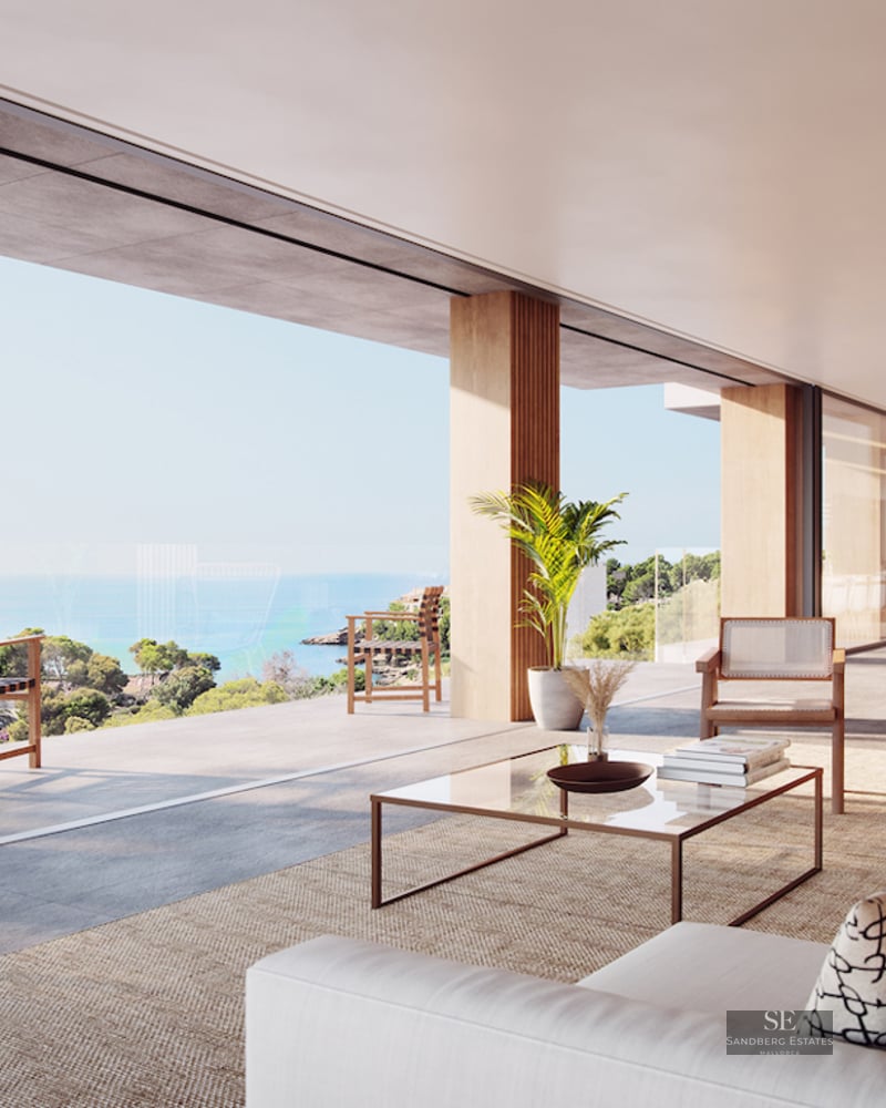 Modern open-plan living room with floor-to-ceiling windows opening to a terrace overlooking the ocean and coast.