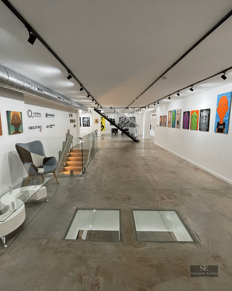 A long industrial gallery with polished concrete floors, white walls filled with pop art, and glass floor inserts.