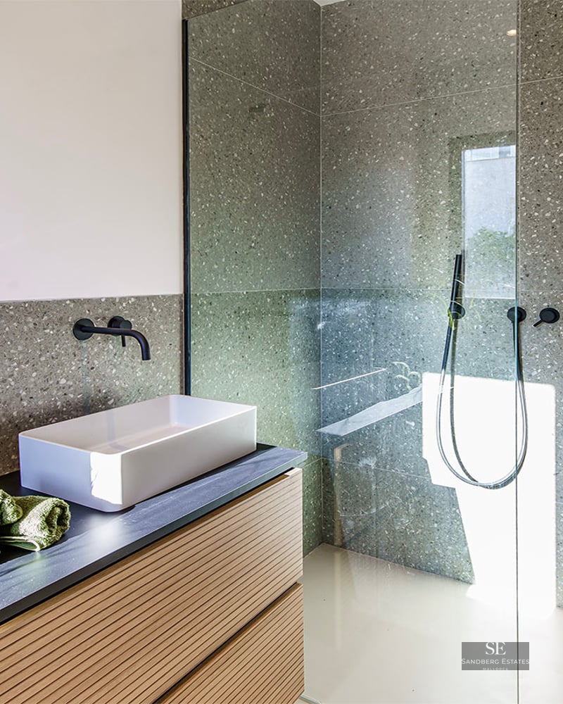 Modern bathroom featuring speckled grey tiles, a white vessel sink on a wooden vanity, and a glass-enclosed shower.