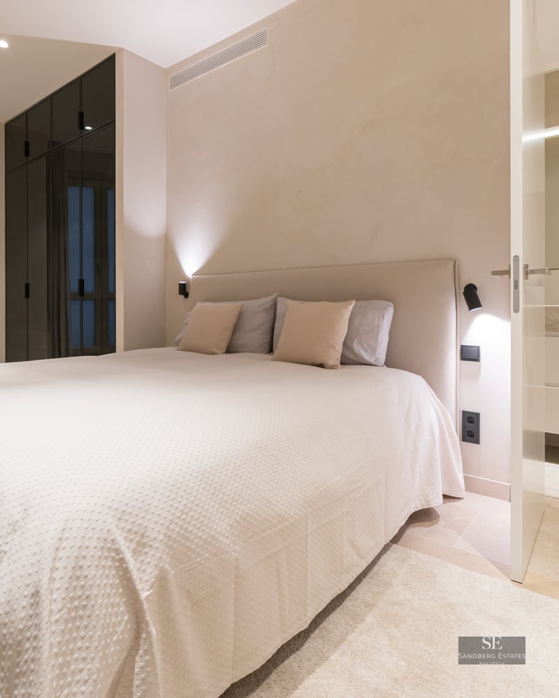A contemporary bedroom featuring a large bed, dark glass wardrobes, and an open door leading to a modern bathroom.