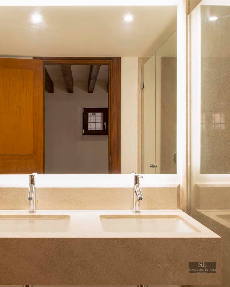 Bathroom with double stone sink, large backlit mirror, and glass shower enclosure.