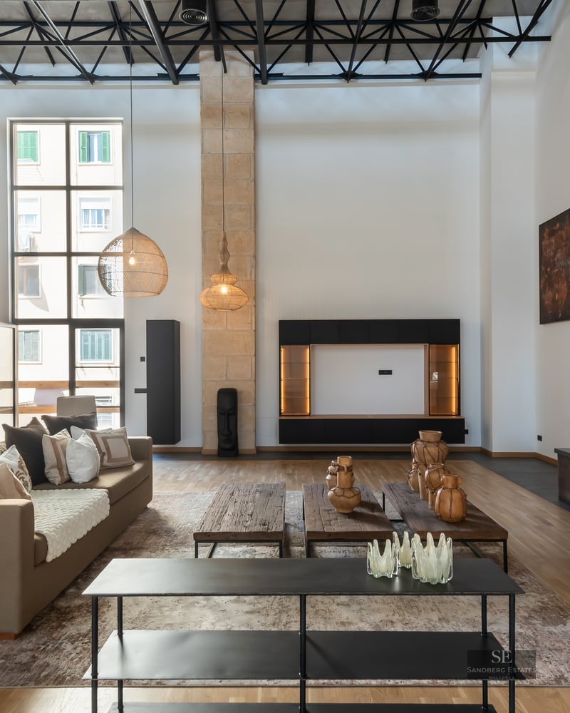 Modern living room with double-height ceilings, beige sofas, metal fireplace, and large wicker pendant lights.