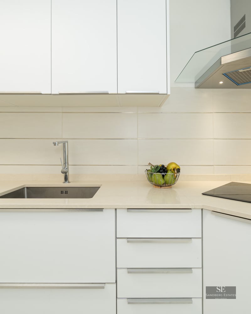 Close-up of a modern white kitchen featuring a stainless steel sink, glass hood, and ceramic cooktop.