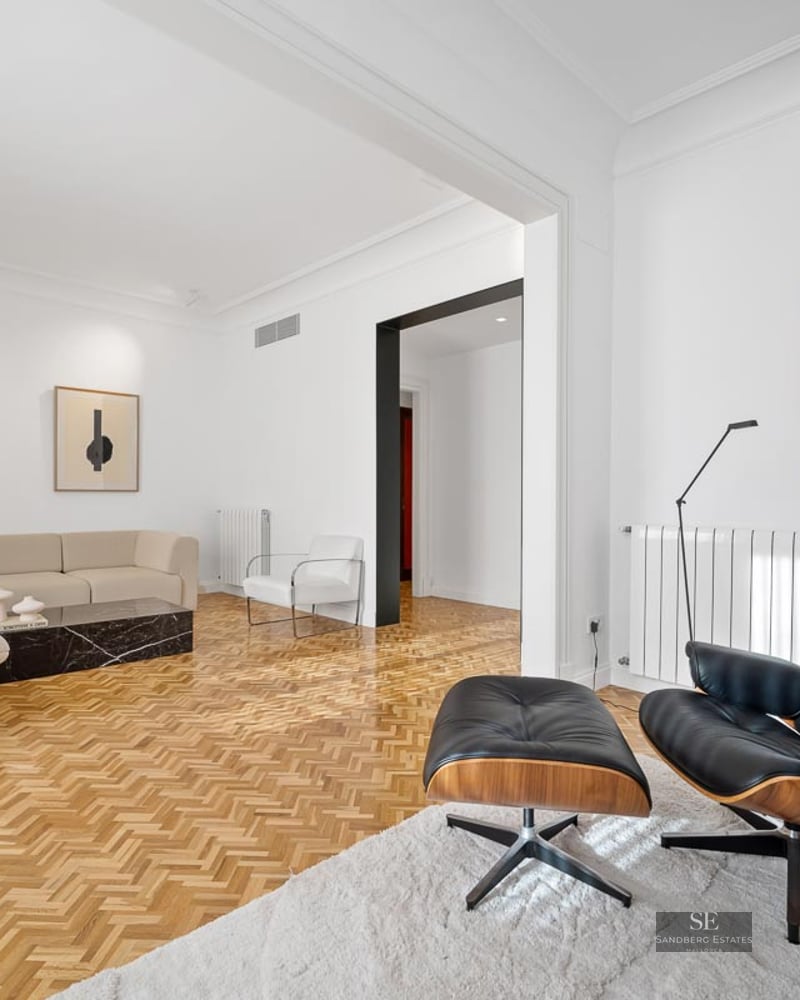 Bright living room featuring a cream sofa, black Eames chair, black marble table, and herringbone wood floors.