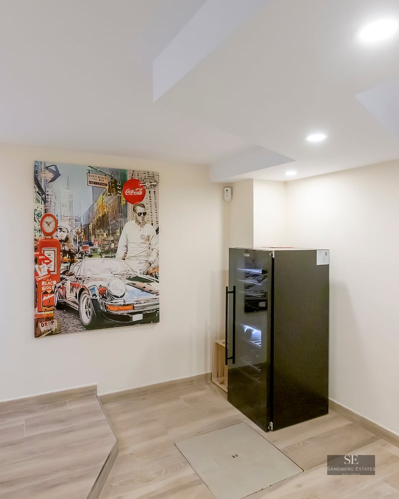 Modern interior landing with a large pop-art painting of a car, a black wine cooler, and glass stairs.