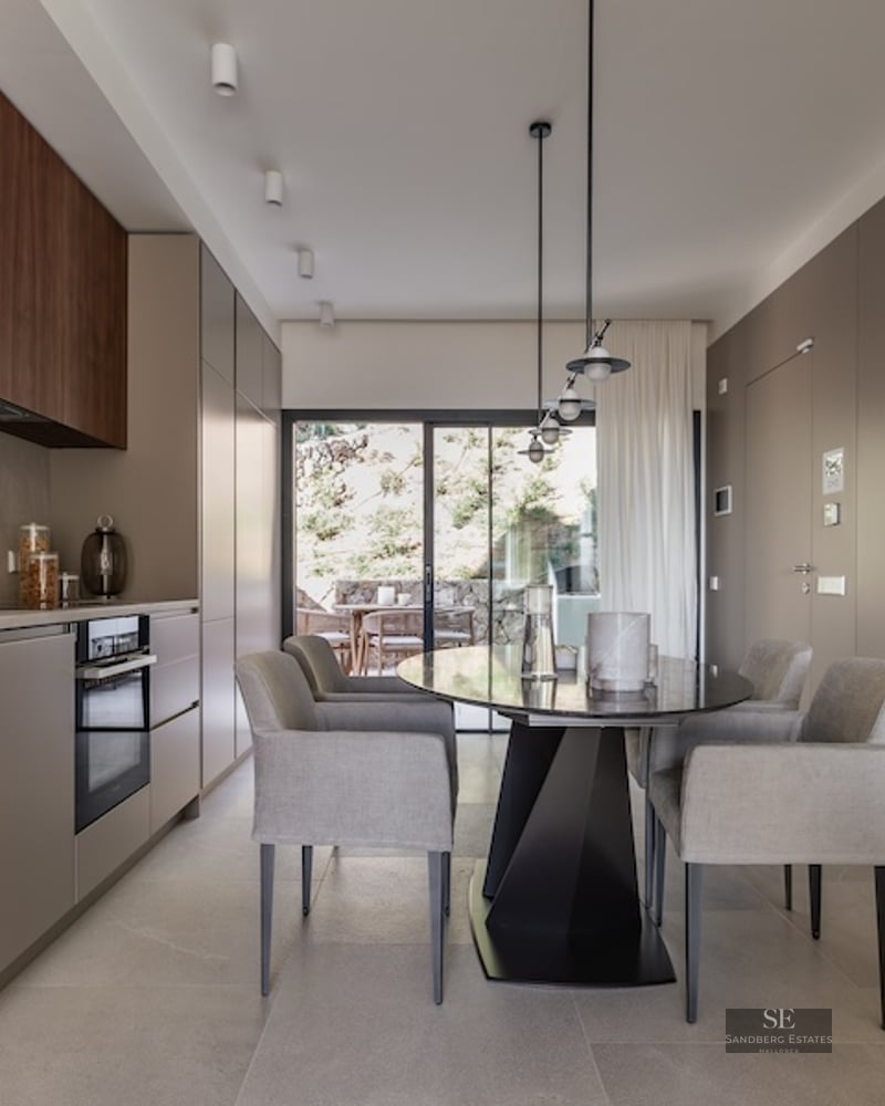 Minimalist kitchen with taupe and wood cabinetry, a grey dining table, and large glass doors leading to a terrace.