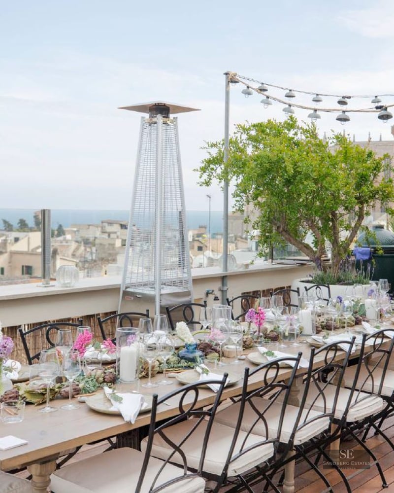 An elegantly set dining table on a wooden deck terrace overlooking a historic city and the sea.