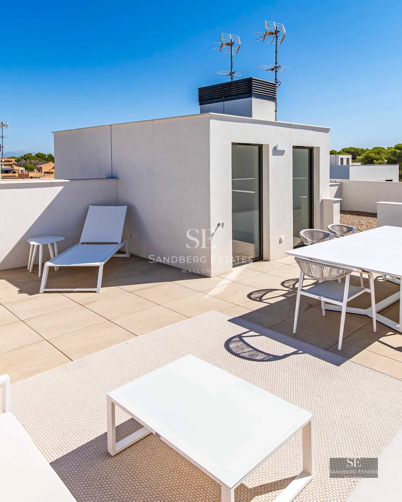 Spacious terrace with wooden flooring, glass railing, panoramic sea view, and modern outdoor furniture. Natural lighting.