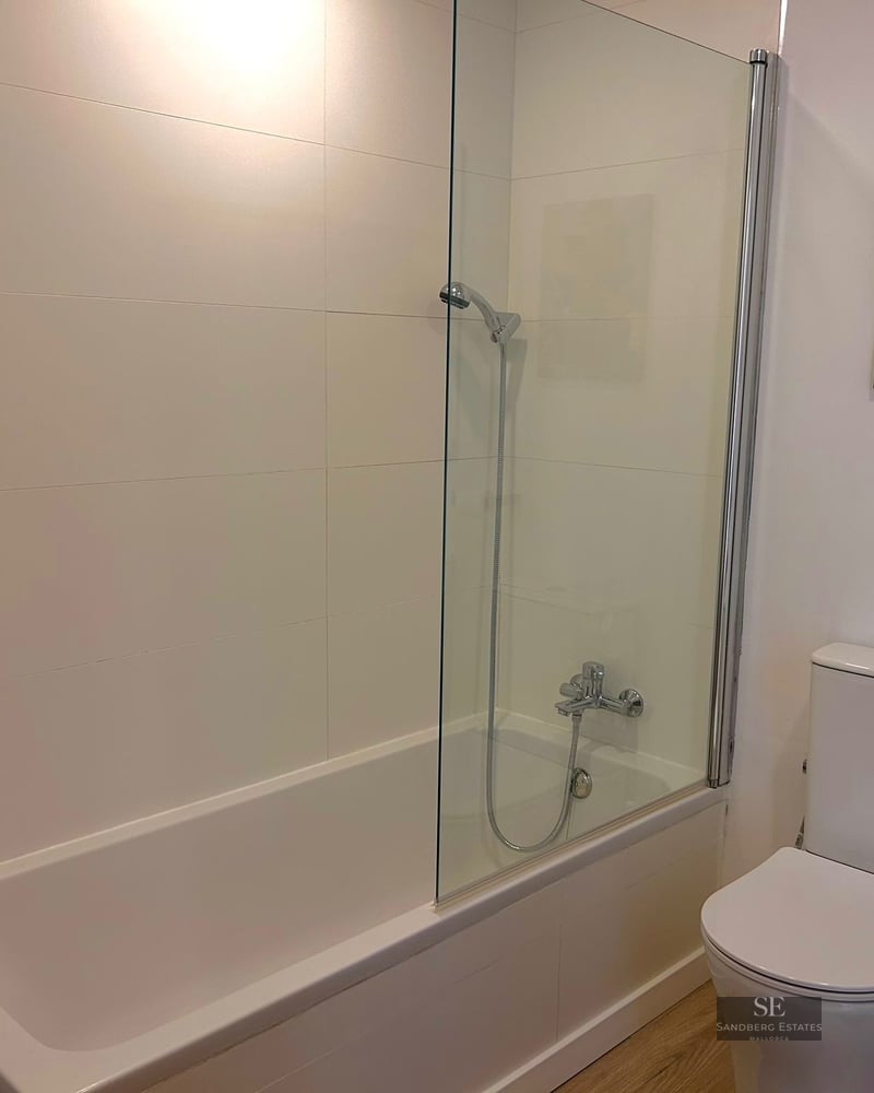 White bathroom featuring a bathtub with glass partition, toilet, and washing machine.
