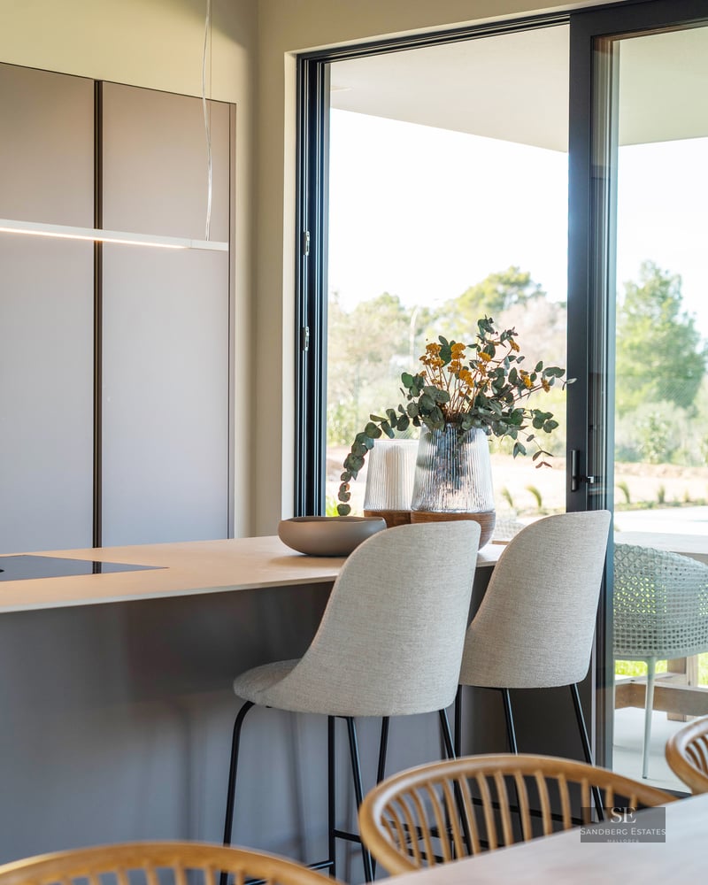 Modern kitchen island with grey bar stools next to a large glass door overlooking a garden.