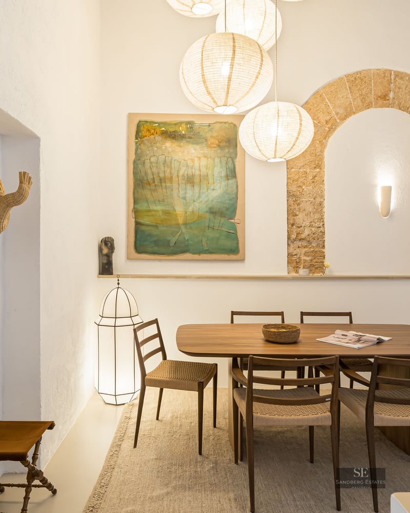 Salle à manger minimaliste avec table en bois sombre, arche en pierre et grandes suspensions en papier.